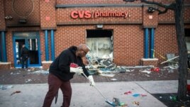 Jerald Miller helps clean up debris from a CVS pharmacy that was set on fire yesterday during rioting after the funeral of Freddie Gray, on April 28, 2015 in Baltimore, Maryland.