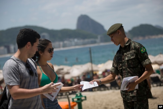 An army soldier distributes a pamphlet about the Aedes aegypti mosquito that spreads the Zika virus on the edge of the Copacabana beach, in Rio de Janeiro, Feb. 13, 2016.