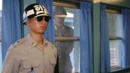 FILE - A North Korean soldier looks through a window as a South Korean stands guard  at the U.N. truce village building that sits on the border of the Demilitarized Zone (DMZ), in Panmunjon, South Korea. 