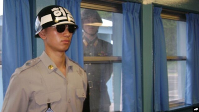 FILE - A North Korean soldier looks through a window as a South Korean stands guard  at the U.N. truce village building that sits on the border of the Demilitarized Zone (DMZ), in Panmunjon, South Korea. 