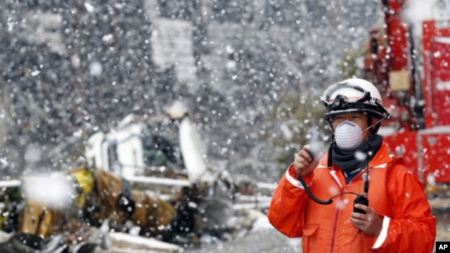 A rescue worker uses a two-way radio transceiver during heavy snowfall at a factory area devastated by an earthquake and tsunami in Sendai, northern Japan, March 16, 2011