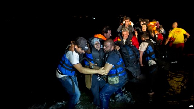 Two Syrian refugees try to carry an elderly woman off a dinghy as it arrives from the Turkish coast to the northeastern Greek island of Lesbos, Oct. 6 , 2015. 