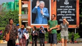 Foreign tourists, right, walk in front of Cambodia's late King Norodom Sihanouk portrait ahead of his funeral, Thursday, Jan. 31, 2013, in Phnom Penh, Cambodia. The body of Sihanouk who died on Oct. 15, 2012 at age 89, is scheduled to be cremated on Feb. 4, 2013. (AP Photo/Heng Sinith)