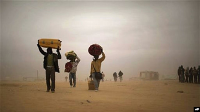 Men, who used to work in Libya and fled the unrest in the country, carry their belongings as they walk during a sand storm in a refugee camp at the Tunisia-Libyan border, in Ras Ajdir, Tunisia, March 15, 2011