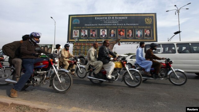 People ride motorcycles past a banner promoting the Eighth D-8 Summit in Islamabad November 21, 2012.