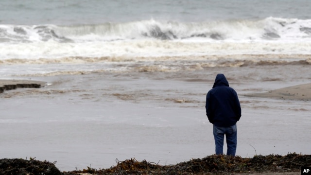 FILE - A man watches ocean waves crash at Seacliff State Beach in Aptos, California.