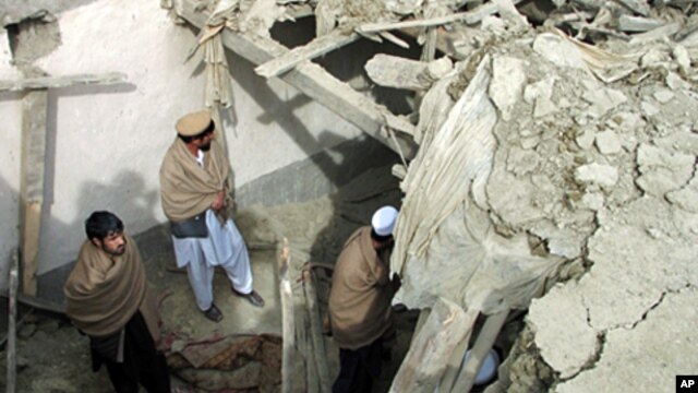 Afghan men stand in the yard of a house that was partly destroyed after an air strike in Nangarhar province, February 21, 2011