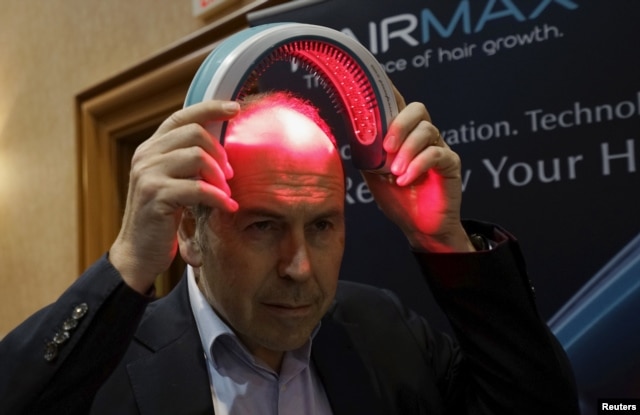 FILE - BBC television reporter Rory Cellan-Jones tries out a HairMax Laserband, a hands-free device described to treat hair loss and cause new hair growth, during the opening event at the Consumer Electronics Show in Las Vegas, Jan. 4, 2016.