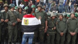 An anti-Mursi protester with an Egyptian flag around his shoulders talks to soldiers standing guard outside the Egyptian presidential palace in Cairo December 9, 2012.