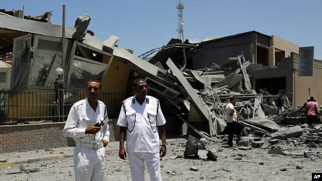 Libyan policemen stand next to a destroyed building that officials said was struck by a NATO airstrike in Tripoli, June 16, 2011