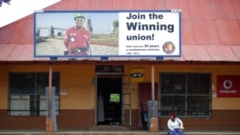 A woman sits beneath a billboard for the National Union of Mineworkers in South Africa's North West province on Oct. 13, 2012.