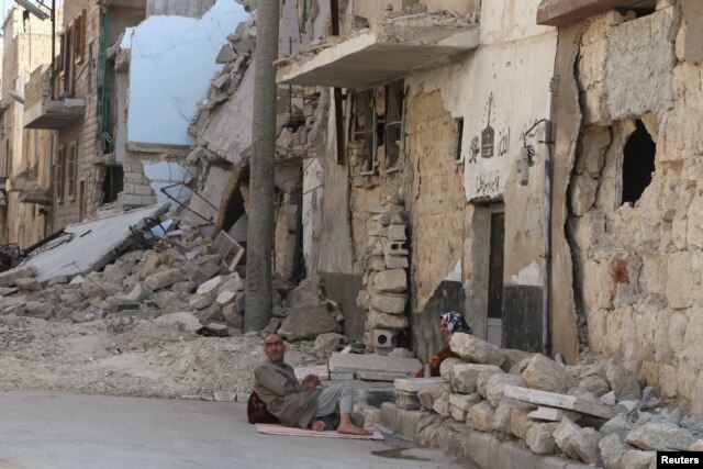 Residents rest on the ground near rubble in a damaged neighbourhood in Aleppo, Syria, July 30, 2015.