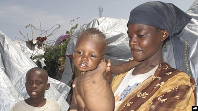 An Somali woman and her children displaced by famine, wait to receive food aid near their makeshift shelters in Mogadishu, Somalia, Friday, July 22, 2011