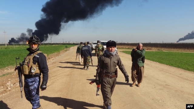 FILE - Members of the Kurdish Peshmerga forces and the Iraqi security forces patrol on a road as smoke billows from the Khubbaz oil field, some 25 km west of the northern city of Kirkuk, Feb. 2, 2015.