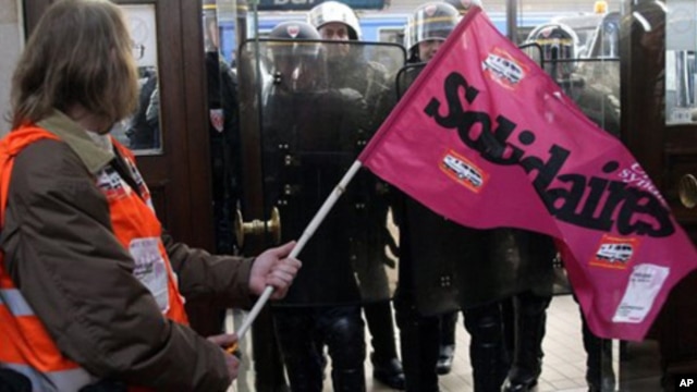 A demonstrator holds a trade union flag as French riot police officers secure the area at the Bordeaux train station, southwest France, Friday Oct. 22, 2010, during a demonstration against President Nicolas Sarkozy's bid to raise the retirement age to 62.