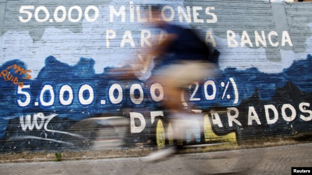 A man rides his bicycle past graffiti that says '50,000 million for rescuing banks and five million unemployed' in Burgos, central Spain, June 28, 2012.  