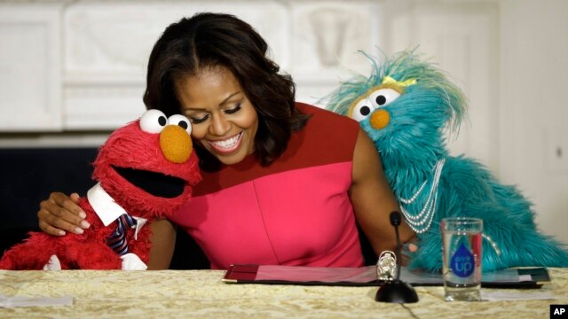 First lady Michelle Obama, center, with PBS Sesame Street's characters Elmo, left, and Rosita, right, as they help promote fresh fruit and vegetable consumption to kids in an event in the State Dining Room of the White House in Washington, file photo.