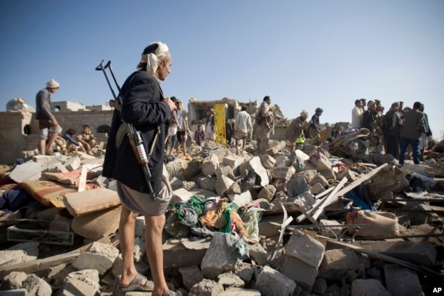 A Houthi Shi'ite fighter stands guard as people search for survivors amid the rubble of houses destroyed by Saudi airstrikes near Sana'a Airport, Yemen, March 26, 2015.