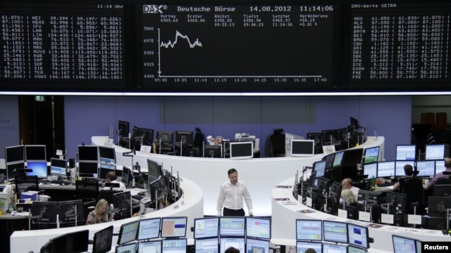 Traders at their desks in front of the DAX board at the Frankfurt stock exchange, August 14, 2012. 