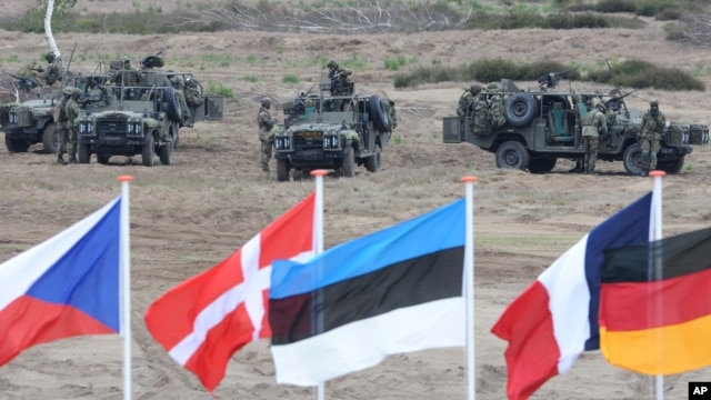 FILE - Flags flutter in front of soldiers taking positions with their army vehicles during the NATO Noble Jump exercise on a training range near Swietoszow Zagan, Poland, June 18, 2015.