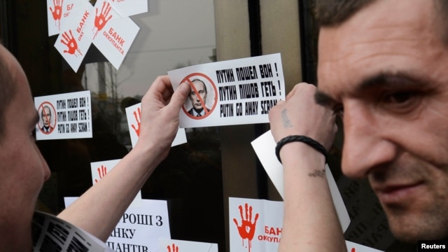 A member of a Ukrainian self-defense unit attaches stickers during a rally outside an office of Alfa bank in Kyiv, March 26, 2014. Participants were demanding that people stop using the services of Alfa bank, which has Russian origin, according to organizers.