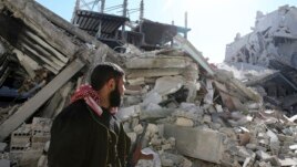 A Free Syrian Army fighter carries his weapon as he walks past damaged buildings in the Arabeen neighborhood of Damascus, Syria, Feb. 12, 2013.