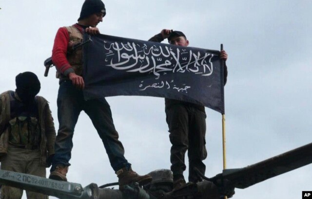 FILE - Rebels from al-Qaida-affiliated Jabhat al-Nusra, also known as the Nusra Front, wave their brigade flag, as they step on the top of a Syrian air force helicopter at Taftanaz air base, Jan. 11, 2013.