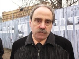 纪念碑人权组织领导人拉钦斯基，他身后的背景是斯大林政治迫害中遭处决人士的画像，以及前克格勃，目前是联邦安全局总部大楼。(美国之音白桦拍摄)