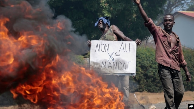 An opposition demonstrator holds a sign in French reading 