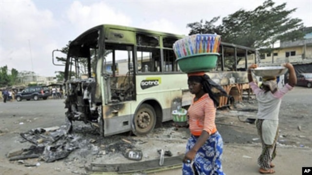 Women carrying loads on their heads walk past a burnt-out bus in Abobo, an Alassane Ouattara stronghold in Abidjan, February 8, 2011
