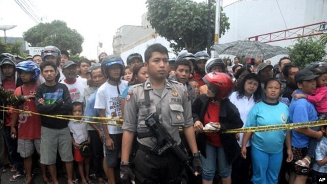 A policeman stands guard as residents watch the site of an explosion in front of a church in Solo, Central Java September 25, 2011.