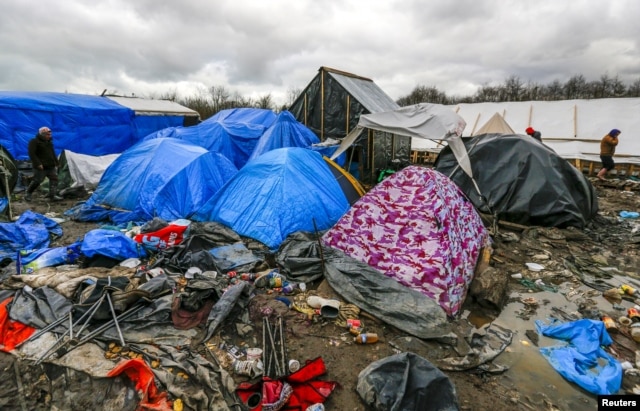 FILE - Migrants walk among tents in a muddy field at a camp of makeshift shelters for migrants and asylum-seekers from Iraq, Kurdistan, Iran and Syria, called the Grande Synthe jungle, near Calais, France, Feb. 3, 2016.