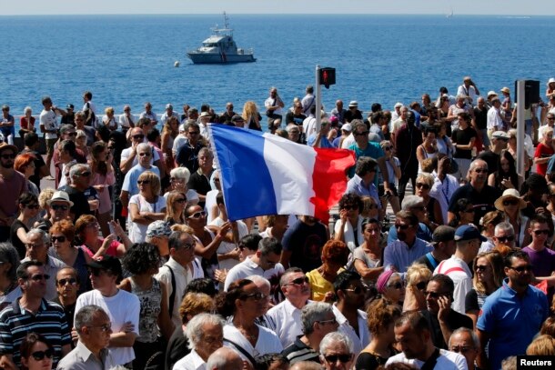 A French flag flies among the crowd as people gather in front of the Monument du Centenaire during a minute of silence on the third day of national mourning to pay tribute to victims of the truck attack along the Promenade des Anglais on Bastille Day that