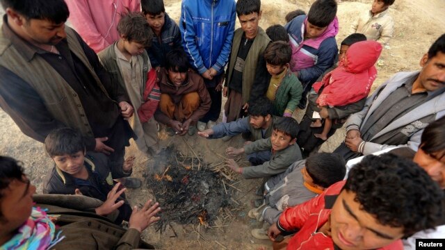 Internally displaced Afghan men and children warm themselves around a fire at a refugee camp on the outskirts of Kabul, December 12, 2012.