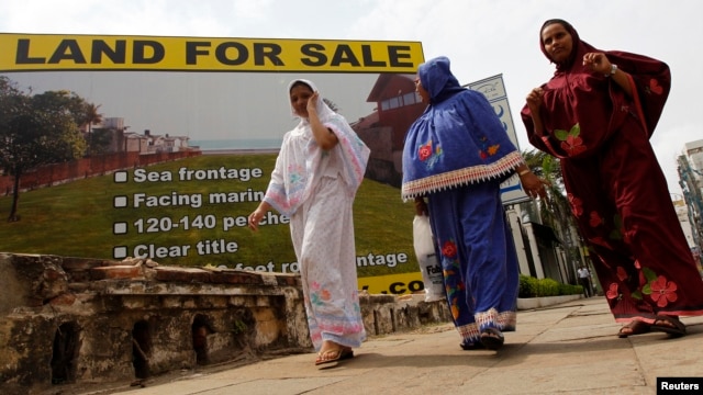 Three women walk past a sign advertising land for sale in Colombo, Sept. 14, 2010.