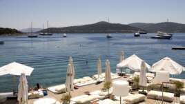 A woman sunbathes on a near-deserted deck as luxury boats are seen anchored off the beach front of a hotel in Golturkbuku, near the resort town of Bodrum on the southwest Aegean coast of Turkey, July 17, 2007. 
