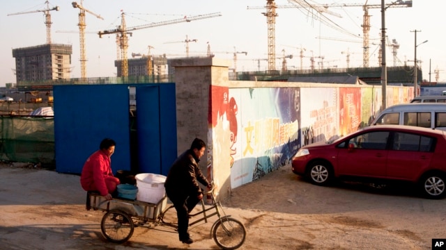 Workers ride a tricycle outside a construction site of a residential real estate project in Beijing, China, January 13, 2013.
