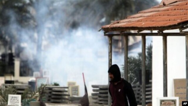 An anti-government protester carrying water to throw on tear gas canisters fired by riot police, moves through a cemetery as gas billows behind him in the Shiite Muslim village of Jidhafs, Bahrain, on the outskirts of the capital of Manama, March 17, 2011