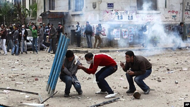 Protesters hide behind a portion of a fence as police fire tear gas and throw stones back at protesters, who have been throwing stones at the police, near Tahrir Square in Cairo Egypt, November 20, 2011.