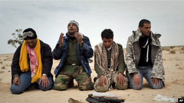 Libyan rebels pray in the desert in front a weapon on the frontline near Sultan, south of Benghazi, March 18, 2011
