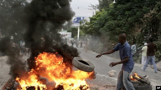 A Haitian throws a tire into fire during a protest following presidential elections in Port-au-Prince, 8 Dec 2010