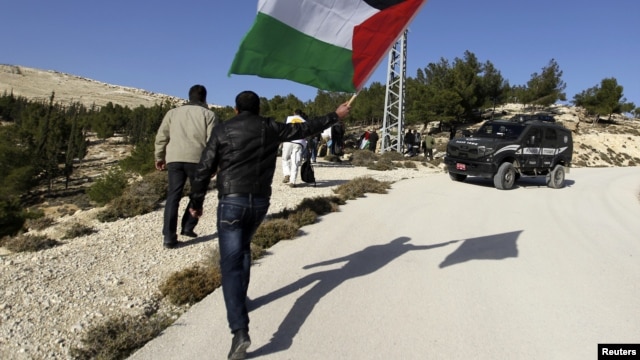 A Palestinian protester holds a flag as he arrives at an area known as 'E1', which connects the two parts of the Israeli-occupied West Bank outside Arab suburbs of East Jerusalem, January 15, 2013.