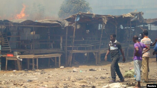 Men stand and watch as a fire rages in the background during clashes between rival gangs in Marche Madina, in Conakry Mar. 1, 2013