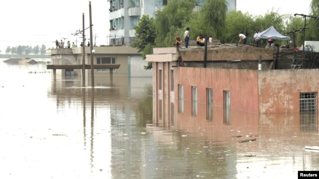 North Koreans are seen on the tops of houses at a flooded village in Anju, July 30, 2012.