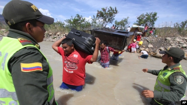 Policías colombianos observan el paso de colombianos deportados que cruzan el río Táchira en la frontera con Venezuela.