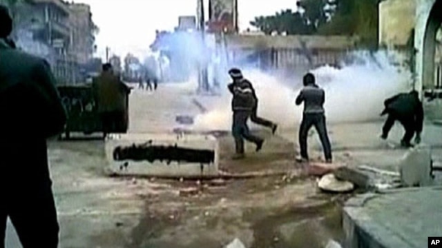 This still image taken from video off a social media website shows protesters covering their faces from tear gas being fired in a Damascus suburb by Syrian security forces, December 30, 2011.