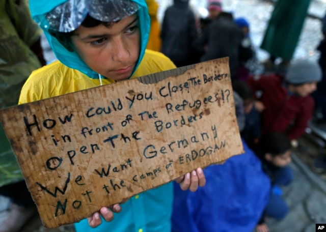 A migrant boy shows a banner saying he wants to travel to Germany rather than camps set up by Turkey, during a protest demanding the opening of the border between Greece and Macedonia in the northern Greek border station of Idomeni, Greece, March 23, 201