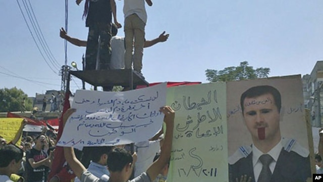 The banners read "The deaf and the blind devil" (l) and "Step down devil" (c), as people protest against Syrian President Bashar al-Assad after Friday prayers in the city of Homs, September 16, 2011.