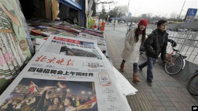 A Chinese couple walks past a newspaper front page showing Egyptians celebrating and title 'Mubarak hands over power' at a newsstand in Beijing, China, February 12, 2011