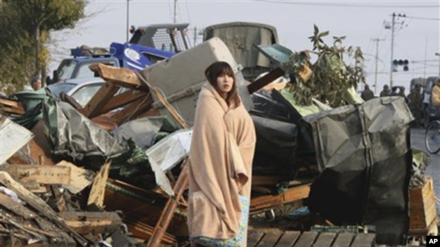 A Japanese woman draped in a blanket stands in the rubble from Friday's quake and tsunami, Sunday, March 13, 2011.